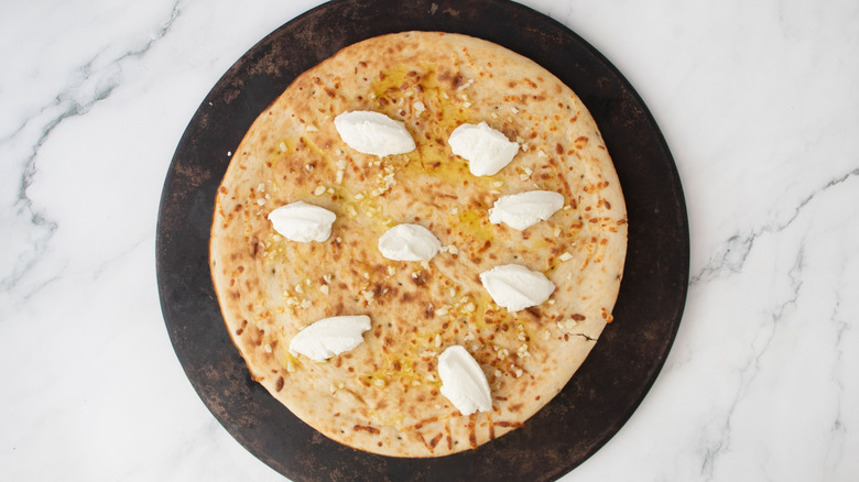 Pizza crust with dollops of ricotta cheese