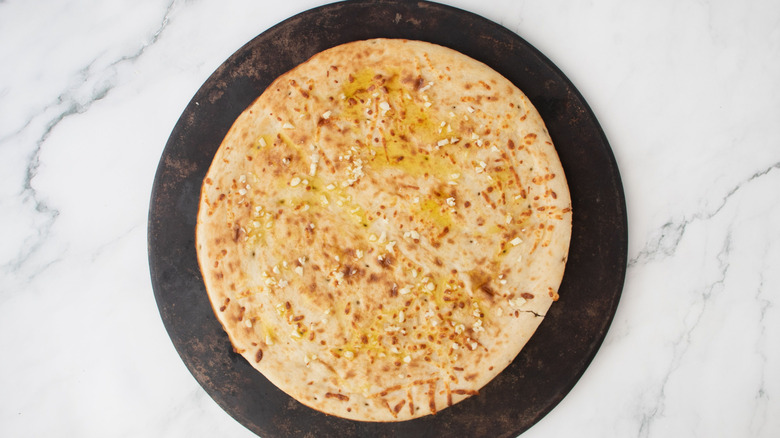 Pizza crust with olive oil and garlic on round baking sheet