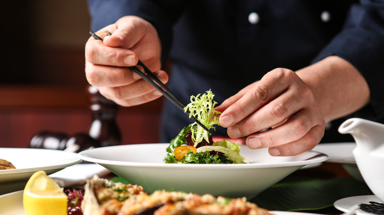 A person finely arranges a salad on a white plate