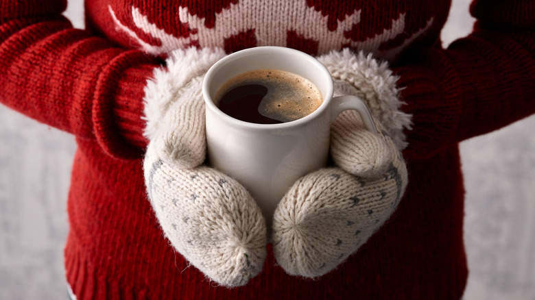 Person in mittens and red sweater holding cup of coffee