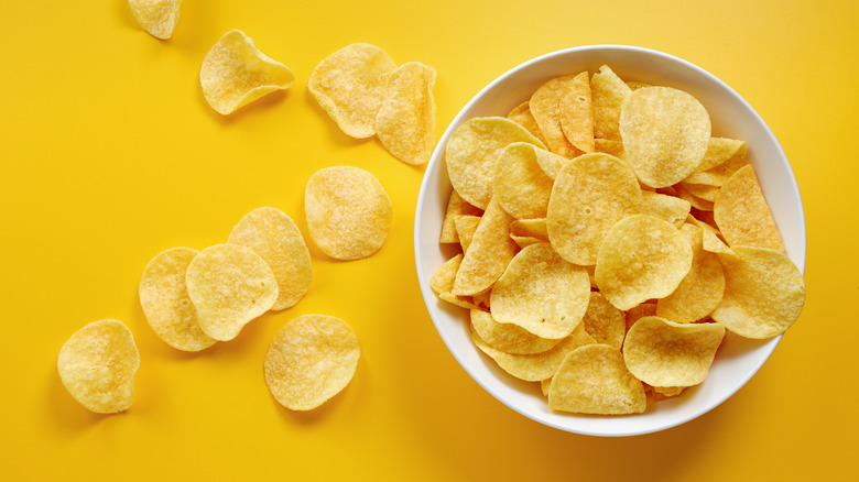 Potato chips in white bowl against yellow background