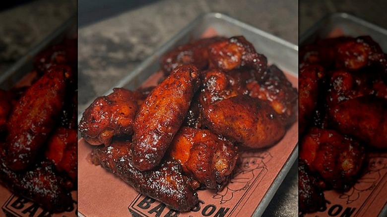 A pile of chicken wings lathered in barbecue sauce sit on a metal platter.