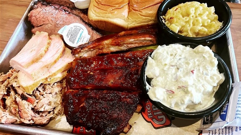 A whole platter of ribs, barbecued meats, bowls of mac and cheese and potato salad, and bread rolls.