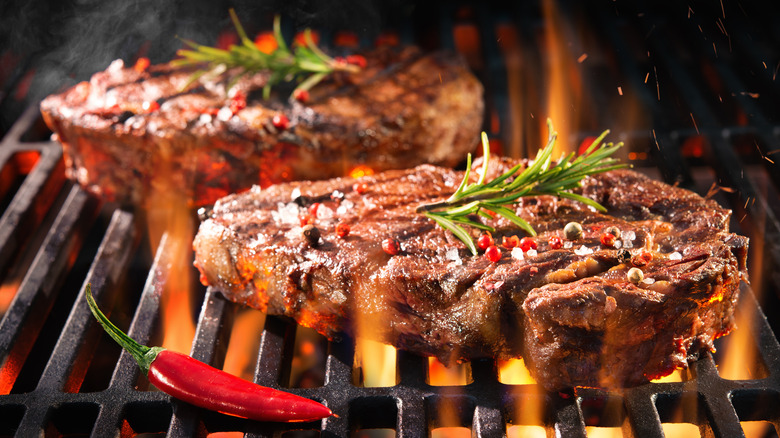 Steak searing on a grill sprinkled with garnish, next to a chile pepper