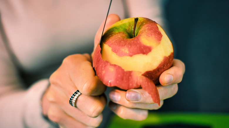 A woman peeling an apple with a knife 