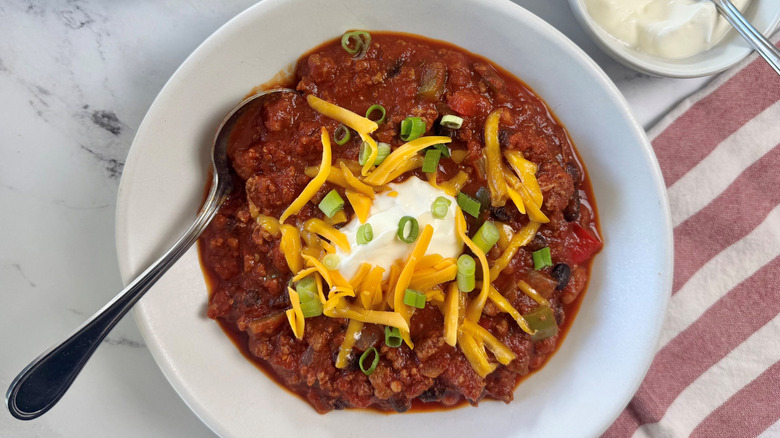 Bowl of chili garnished with sour cream, cheese, and green onions