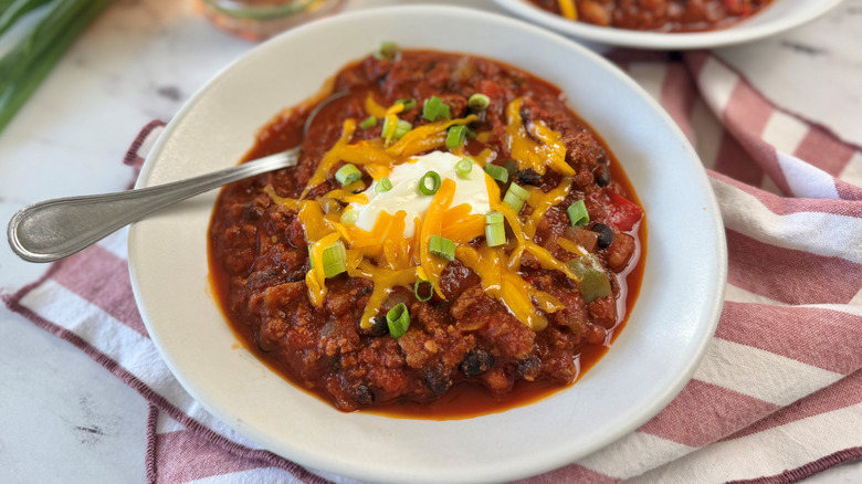 Chili serving in bowl topped with sour cream, cheese, and green onions