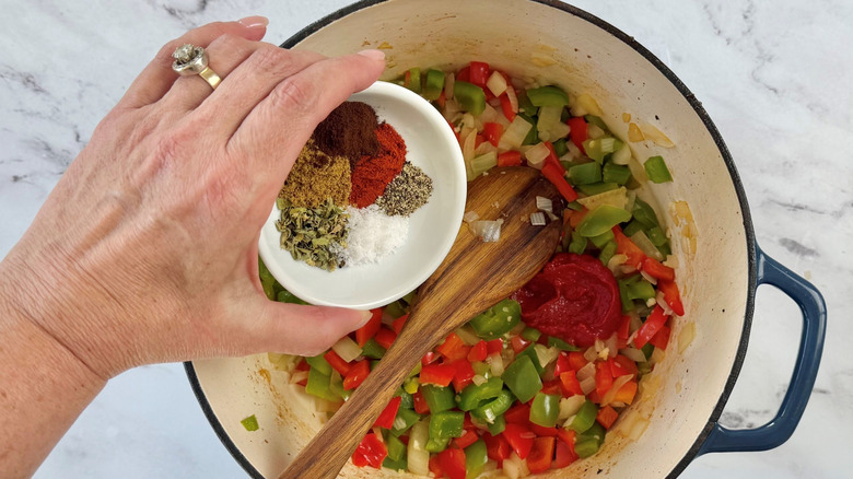 Hand adding small bowl with various seasonings to pot