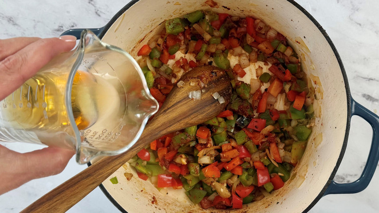 Pouring bourbon into pot with sauteed and seasoned vegetables