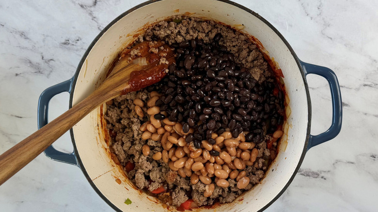 Beef and beans in pot with wooden spoon