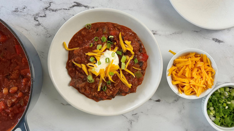 Bowl of garnished chili next to smaller bowl of cheese and green onions