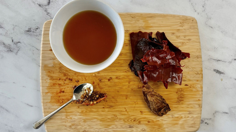 Bowl of soaking liquid with seeded and stemmed chiles on wooden board