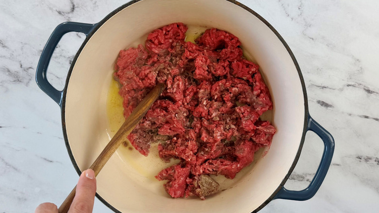 Wooden spoon breaking up ground beef in pot