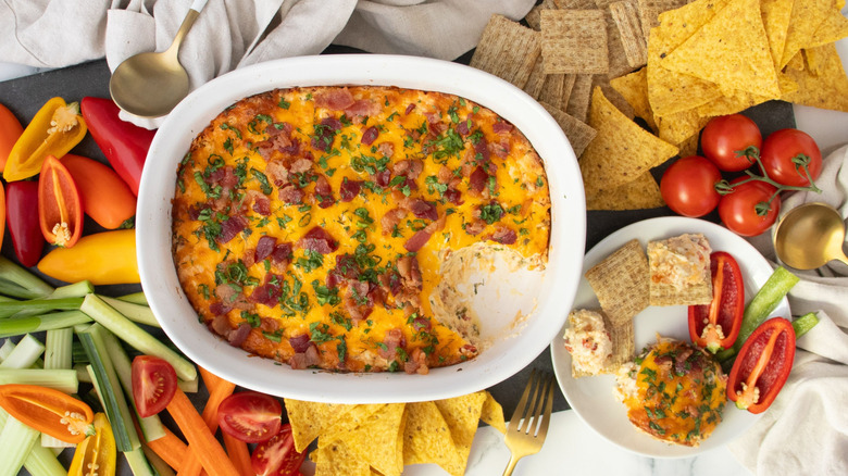 Chicken bacon ranch dip in casserole dish surrounded by crudites, crackers, and chips