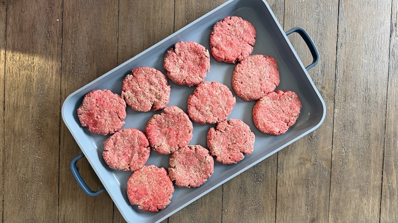 Uncooked burger patties in baking dish on wooden table.