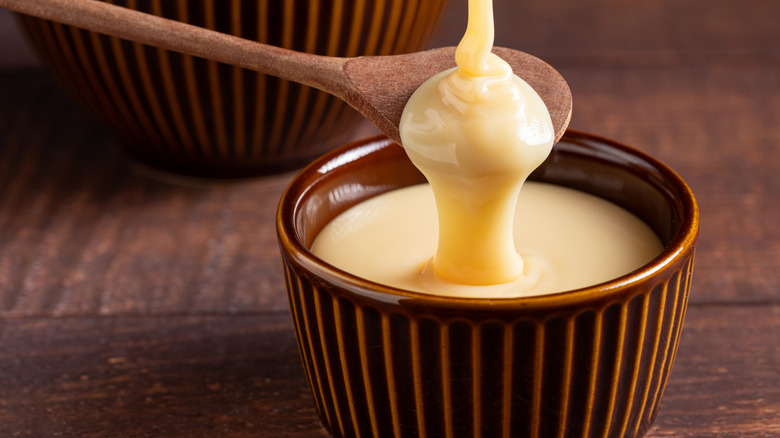 Sweetened condensed milk pouring over spoon and into brown ramekin