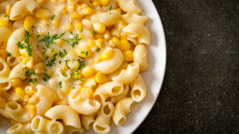 Cream corn mixed into mac and cheese on white plate.