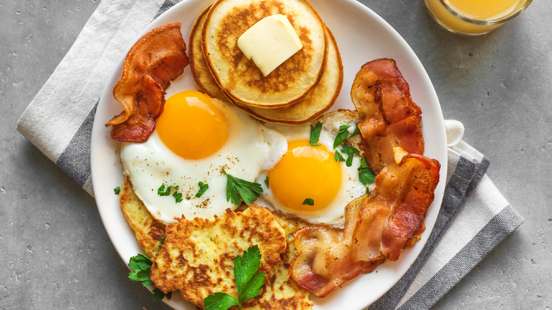 Fried eggs, silver dollar pancakes, bacon, and hash browns on a plate