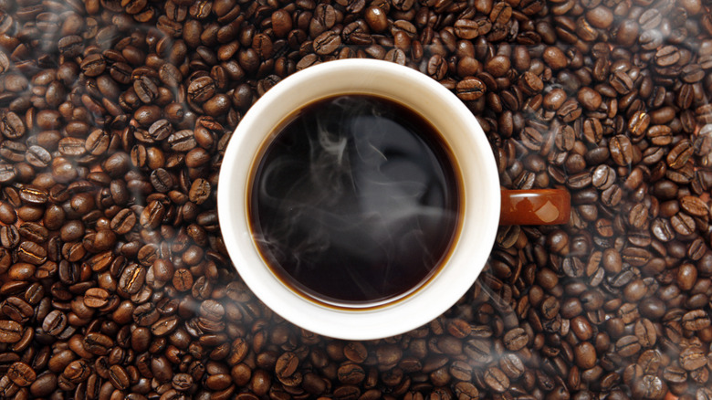 Birds eye view of hot coffee mug sitting on coffee beans