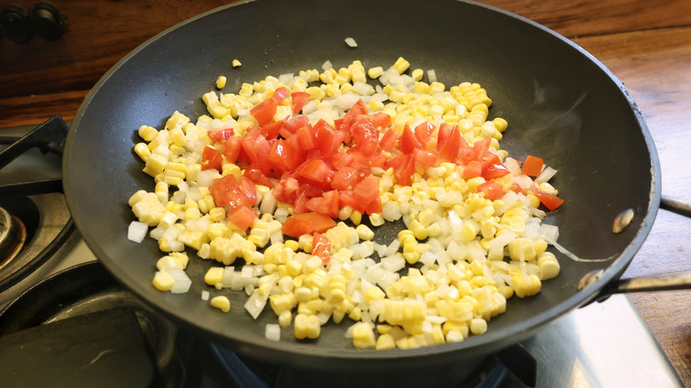 skillet with corn, onions, and tomatoes in it