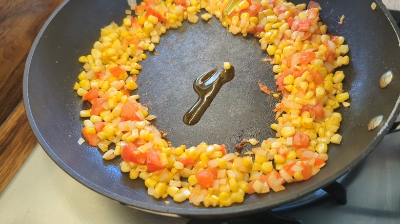 skillet with corn, tomatoes, and onions pushed to outside and oil in the center