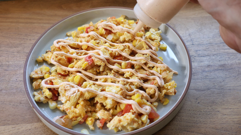squeeze bottle dispensing creamy sauce onto egg scramvle with corn, tomatoes, and onions