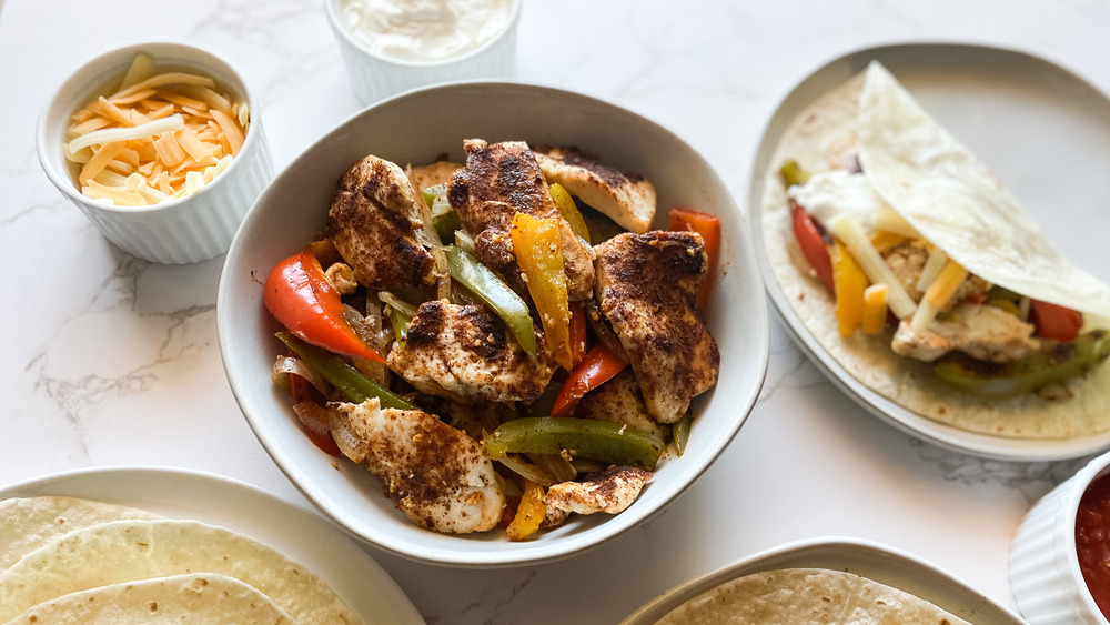finished chicken fajitas with bell peppers onions cheese sour cream and salsa