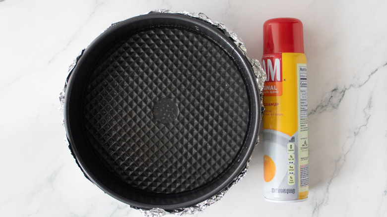 Foil-wrapped springform pan next to can of Pam spray