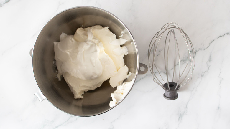 Sour cream and cream cheese in mixer bowl next to whisk attachment