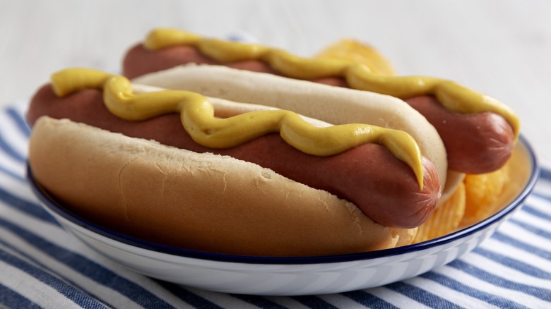 Two hot dogs with mustard on plate.