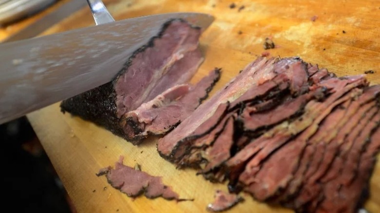 Knife slicing pastrami on board