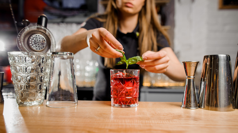 Bartender garnishing vodka cranberry with mint leaves.