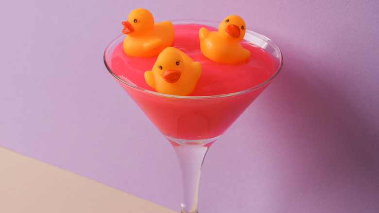 Rubber ducks swimming in pink liquid in martini glass.