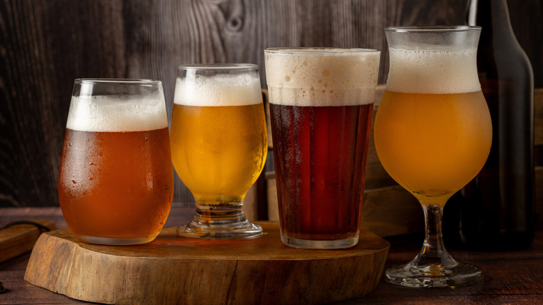 Four glasses filled with various types of beer on wooden slab