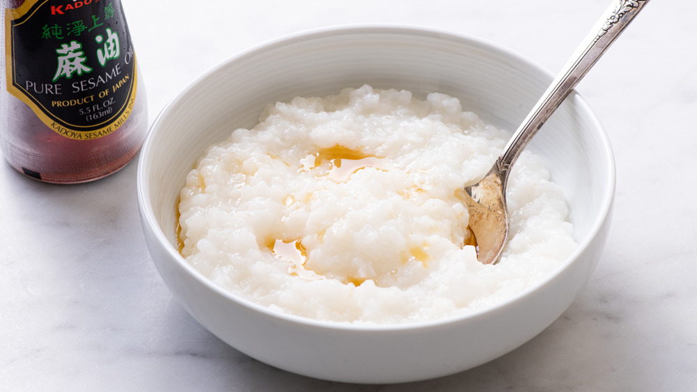 Congee in a white bowl next to sesame oil
