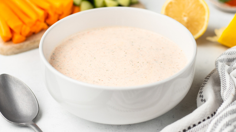 Copycat Popeyes blackened ranch sauce in white bowl in front of carrot and cucumber sticks