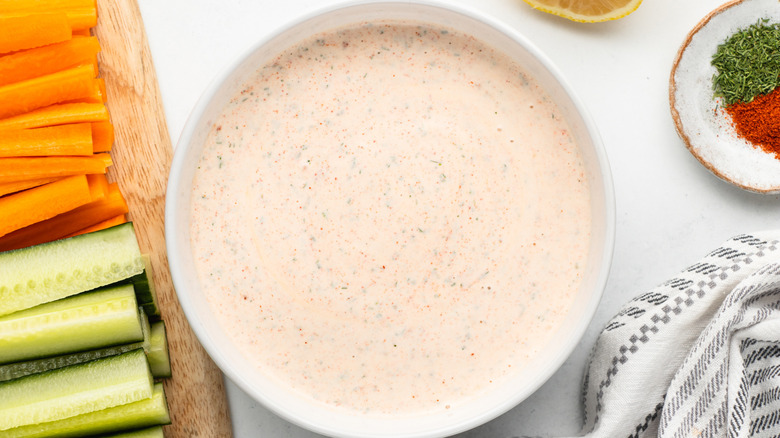 Bowl of copycat Popeyes blackened ranch sauce next to carrot and cucumber sticks