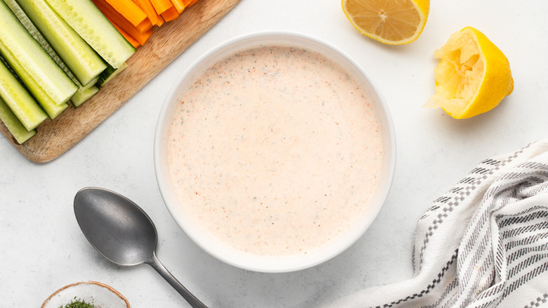 Bowl of copycat Popeyes blackened ranch sauce next to crudites and sliced lemon