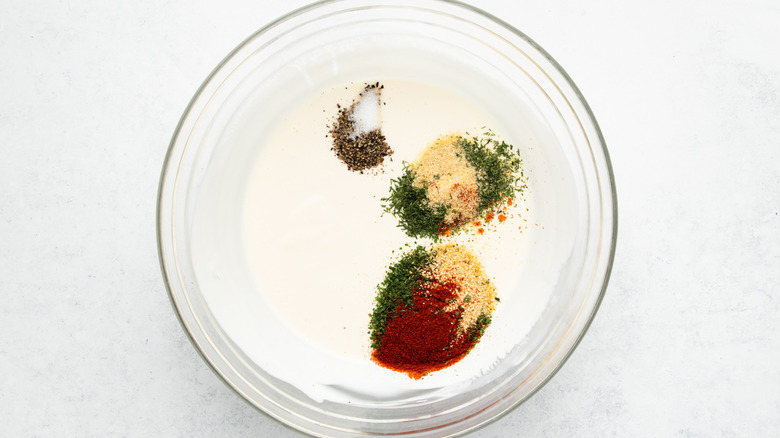 Sour cream mixture and various seasonings in glass mixing bowl