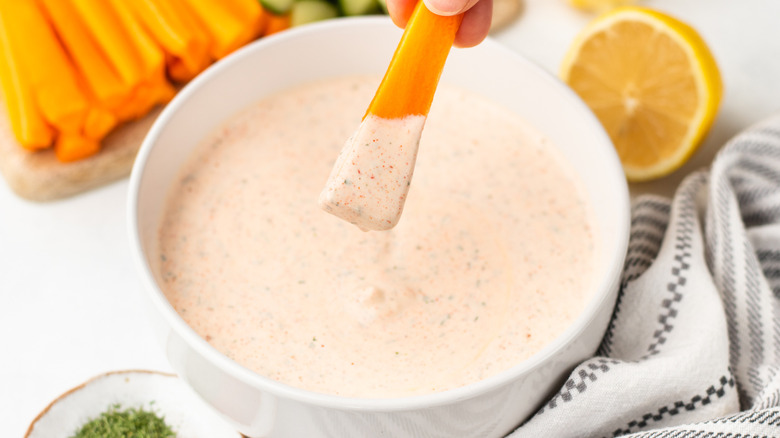 Dipping carrot stick into bowl of copycat Popeyes blackened ranch sauce