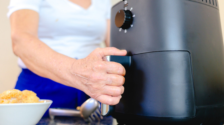 Hand grabbing handle to air fryer basket