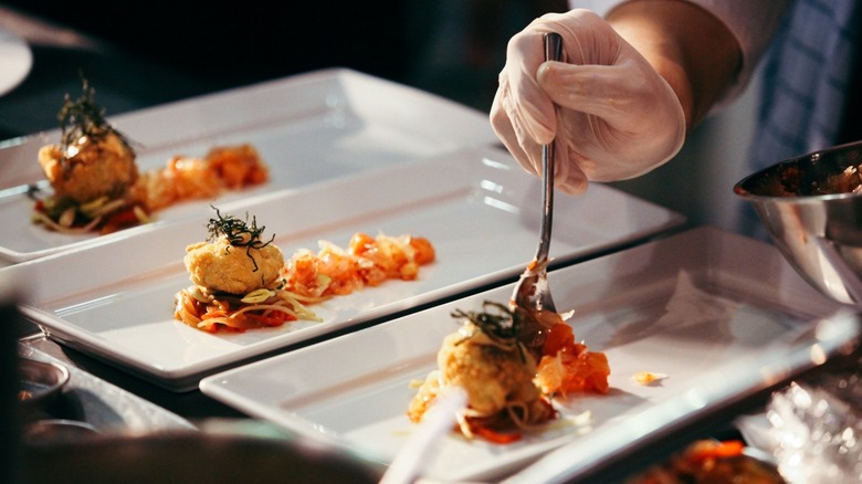A gloved hand plating food
