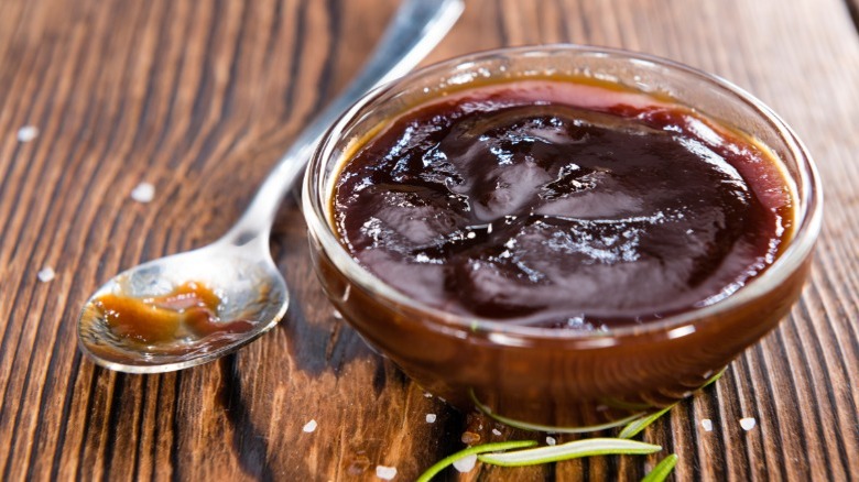 Glass bowl of barbecue sauce with spoon on wooden table