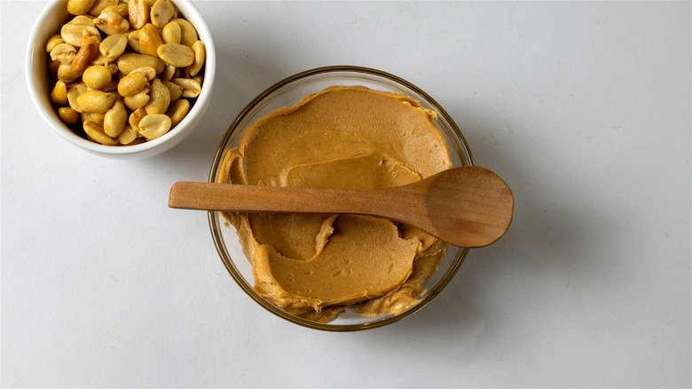 Freshly made peanut butter and a wooden spoon, next to a bowl of roasted peanuts.