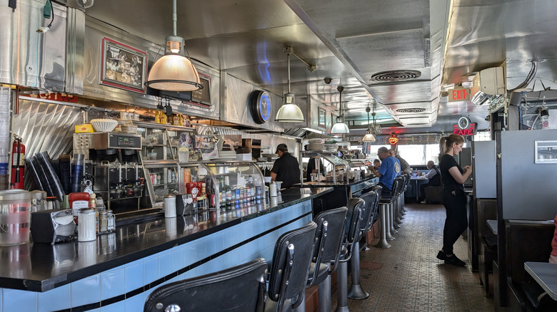 The interior of the Deluxe Town Diner in Massachusetts with a row of bar seating and chrome walls