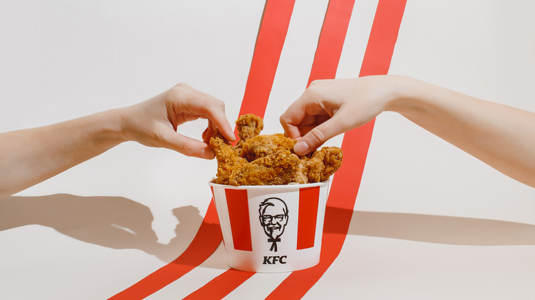 KFC chicken in a bucket with two hands taking pieces