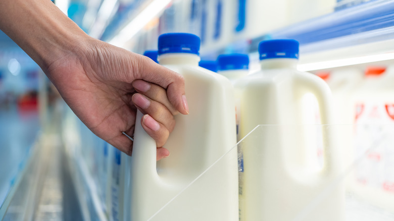 Hand grabbing half gallon of milk from grocery store shelf.