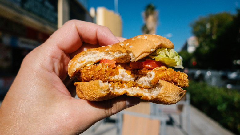 Person holding chicken sandwich outside on city street