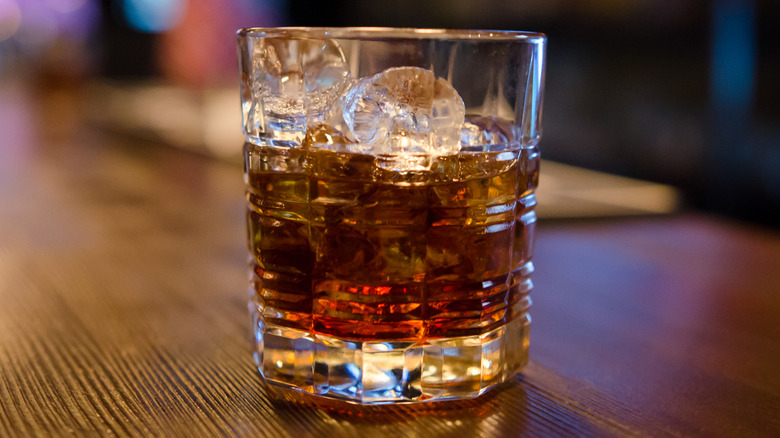 Coca Cola and whiskey on ice in low glass on wooden bar