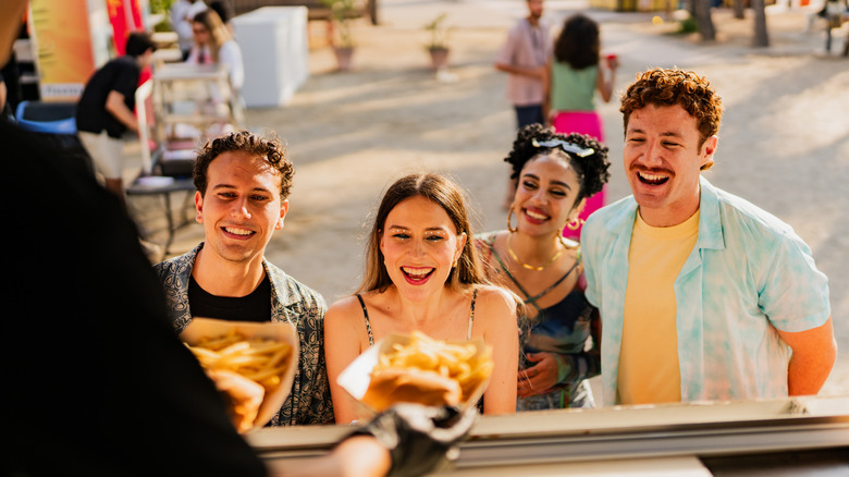 Four people smiling outside food truck window while food is presented